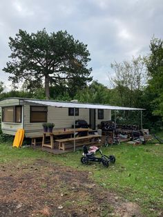 an rv parked in the grass next to a picnic table and bike with a canopy over it