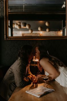 two people sitting at a table kissing each other