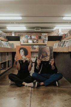 two people sitting on the floor holding up pictures in front of their faces and looking at them