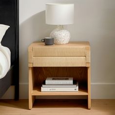 a nightstand with books and a cup on it next to a lamp in a bedroom