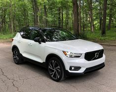 a white volvo suv parked in front of some trees