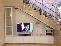 a flat screen tv sitting on top of a white cabinet next to a stair case