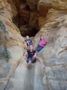 three people sitting on some rocks in the middle of a canyon, posing for a photo