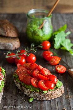 two pieces of bread topped with tomatoes and lettuce next to a jar of pesto