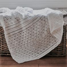 a white crocheted blanket sitting on top of a wooden floor next to a basket