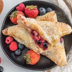 two pastries on a black plate with berries and blueberries next to each other