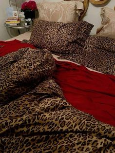 a leopard print comforter on a bed with red sheets and pillows, in front of a mirror