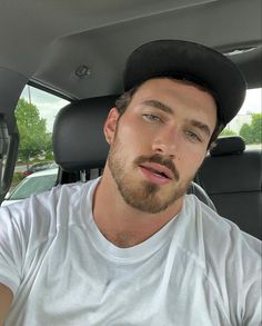 a man sitting in the back seat of a car wearing a black hat and white t - shirt