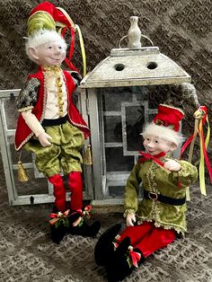 two old fashioned dolls sitting next to each other on a carpeted floor in front of a lantern