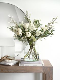 a vase filled with white flowers sitting on top of a table next to a mirror