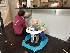 a man kneeling down next to a baby sitting in a high chair on top of a hard wood floor