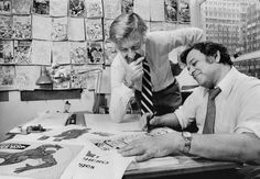 two men sitting at a table working on comics