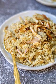 a white plate topped with rice and almonds next to a gold spoon on top of a table