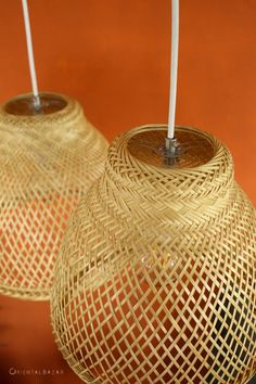 two wicker lamps with white candles in them on an orange background, one is lit and the other is closed