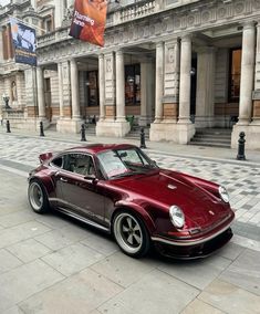 a red car parked on the side of a road in front of a tall building