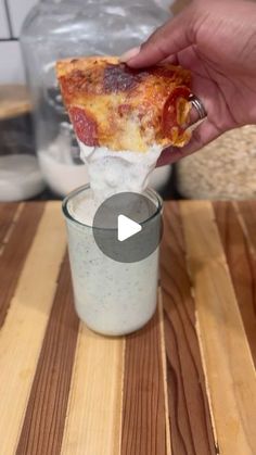 a person holding up a piece of pizza in a glass on top of a wooden table