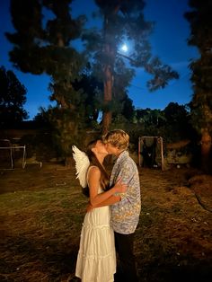 a man and woman kissing in front of a tree with the moon shining behind them