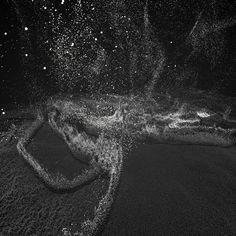 black and white photograph of water splashing on the beach with stars in the sky