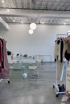 an empty room with clothes hanging on racks and chairs in front of the glass table