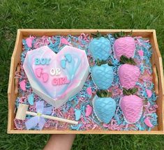 a box filled with blue and pink frosted strawberries next to a heart shaped cake