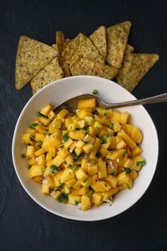 a white bowl filled with mango salsa next to tortilla chips on a black surface