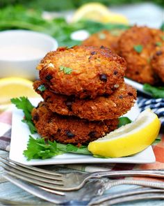 three fried crab cakes on a plate with lemon wedges and garnishes