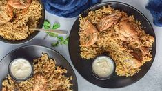 three plates filled with rice and meat on top of a white tablecloth next to blue napkins