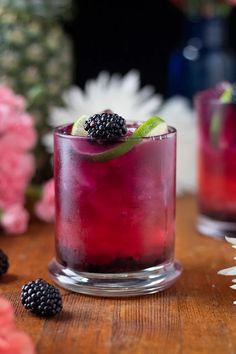 two glasses filled with blackberry lemonade and blackberries on top of a wooden table