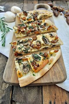 four slices of pizza sitting on top of a wooden cutting board next to garlic and mushrooms