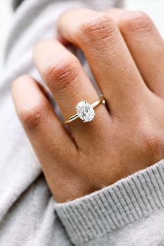 a woman's hand wearing a gold ring with a white diamond on the middle