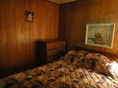 a bed in a room with wood paneling and a painting on the wall above it