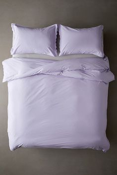 an unmade bed with two pillows and purple comforter on the bottom half, in front of a gray wall