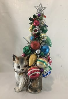 a small christmas tree with ornaments on it and a cat figurine next to it