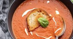 a bowl of tomato soup with bread and basil leaves on the side, ready to be eaten