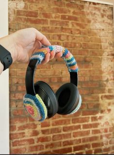 a person holding up some headphones in front of a brick wall