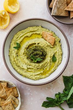 a bowl filled with hummus next to crackers and lemon wedges on the side