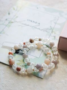 a bracelet with pearls and glass beads on a table next to a pink card box