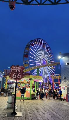 the ferris wheel is lit up at night with people walking around it and on the boardwalk