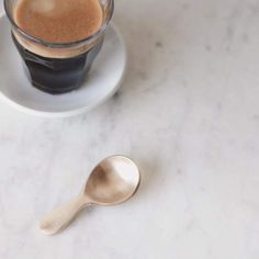 a cup of coffee on a saucer next to a spoon with liquid in it