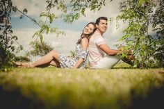 a man and woman sitting on the grass under trees