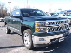 a green truck parked in a parking lot next to other cars and trucks behind it