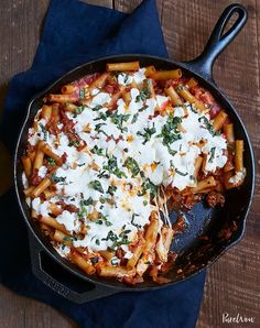 a skillet filled with pasta and cheese on top of a blue cloth next to a wooden table