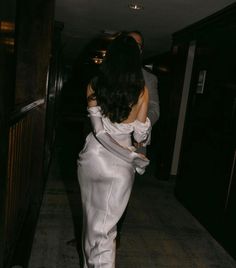 a woman in a white dress is walking down the hallway with her back to the camera