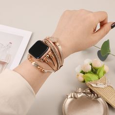 a woman's hand holding an apple watch on her wrist with multiple bracelets