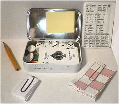 an open tin box with some cards and pens on the table next to it,