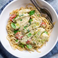 a white bowl filled with pasta covered in pesto sauce and topped with chicken breast