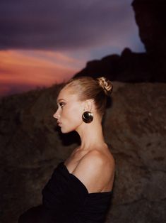 a woman in a black dress with large earrings on her head looking off into the distance