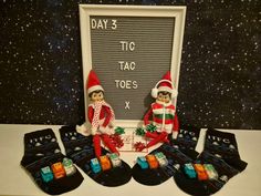 two elfs sitting next to each other in front of a chalkboard with the words day 3 tic toe's written on it