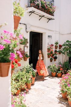 a woman in an orange dress is walking into a building with potted plants and flowers