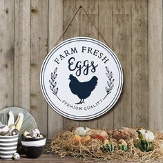 a farm fresh eggs sign hanging on the side of a wooden wall next to hay